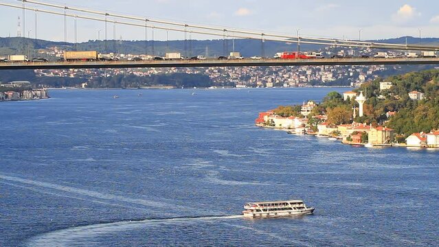 Aerial view of Bosphorus with a static camera and tele lens. Heavy bus and truck traffic on suspension bridge FSM and passenger motorboat sailing slowly towards Kandilli, Asian side of Istanbul City
