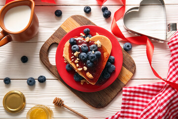 Plate with tasty pancakes in shape of heart, blueberry and jam on light wooden background. Valentine's Day celebration
