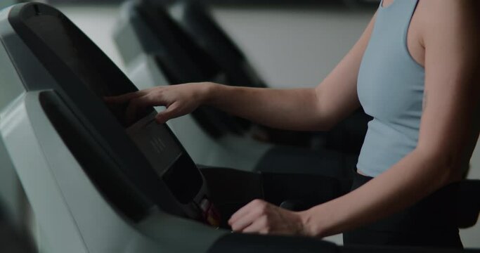 Treadmill workout at indoor fitness gym. Fitness woman running on a treadmill in the gym. Athlete uses a running machine in a fitness center. Pretty girl doing cardio training in a sports club. 4K
