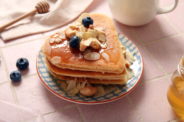 Plate with tasty pancakes in shape of heart, blueberry and nuts on pink tile background, closeup. Valentine's Day celebration