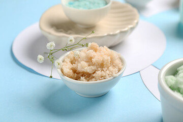 Bowl with scrub and flowers on blue background, closeup. Body massage concept