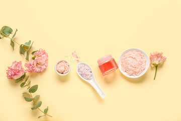 Scrubs with sea salt, cosmetic oil and flowers on light yellow background. Body massage concept