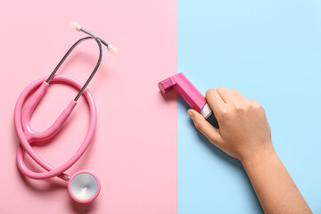 Child's hand with asthma inhaler and stethoscope on color background