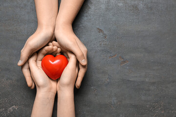 Hands of woman and child with red heart on black background