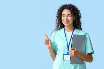 Female African-American medical intern with laptop pointing at something on blue background