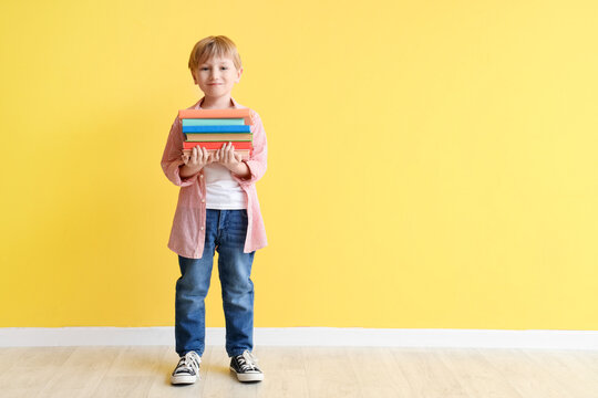 Cute little boy with stack of books against yellow wall