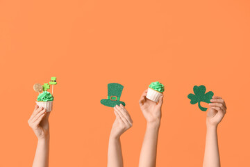 Female hands with tasty cupcakes and decor for St. Patrick's Day on orange background