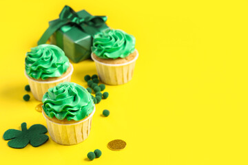 Tasty green cupcakes with gift box and decor for St. Patrick's Day on yellow background