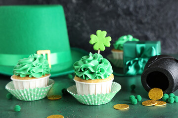 Tasty cupcakes with leprechaun hat and decor for St. Patrick's Day on green grunge table against...