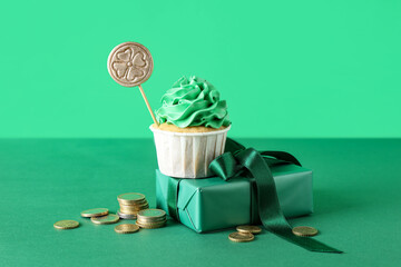Tasty cupcake with gift box and golden coins for St. Patrick's Day on green background