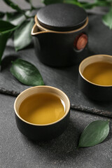 Board with teapot, cups of tea and leaves on black grunge background