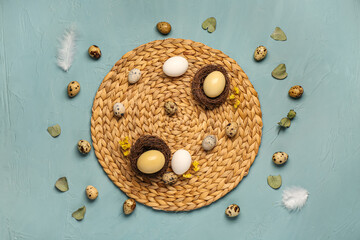 Straw mat with Easter eggs, flowers and leaves on blue background