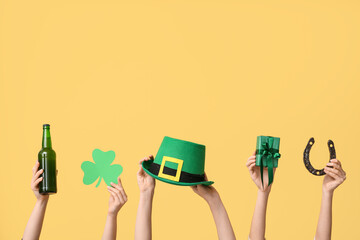 Female hands holding beer and party decor for St. Patrick's Day celebration on yellow background