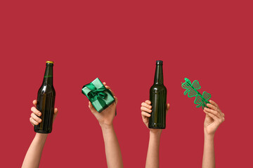 Female hands holding beer, gift box and novelty glasses on red background. St. Patrick's Day...
