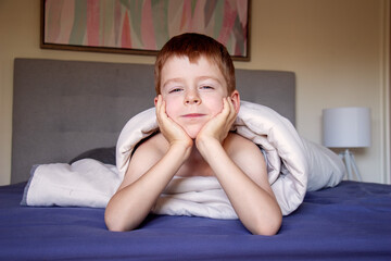 A junior high school boy is lying in bed wrapped in a blanket