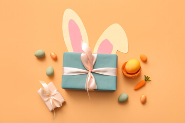 Easter eggs with gift boxes and paper bunny ears on orange background