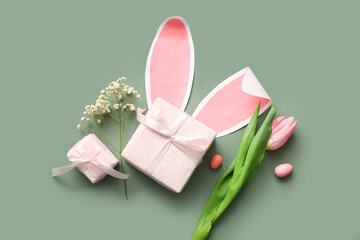 Easter eggs with gift boxes and paper bunny ears on green background