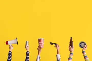 Zelfklevend Fotobehang Many hands with bucket of popcorn, drinks and megaphone on yellow background © Pixel-Shot