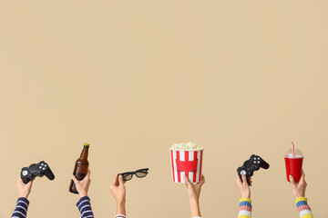 Many hands with bucket of popcorn, drinks and game pads on beige background
