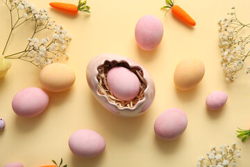 Holder with Easter eggs, carrots and gypsophila flowers on beige background