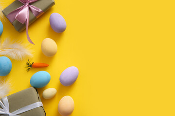 Painted Easter eggs with feathers and gift boxes on yellow background