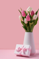 Vase with beautiful tulips and gift box on pink background. International Women's Day