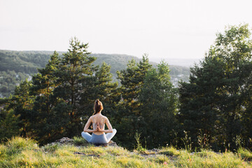 Naklejka premium Rear view beautiful young woman practicing yoga on rock in summer forest outdoor.