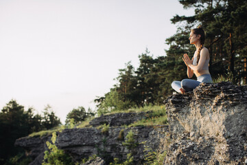 Naklejka na ściany i meble A young woman practices yoga and meditates in the mountains at sunset. Peace and unity with nature.