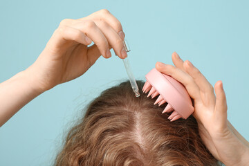 Naklejka premium Young woman using hair scalp massager with cosmetic oil on blue background, closeup