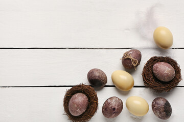 Obraz premium Nests with painted Easter eggs and feathers on white wooden background