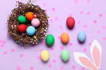 Composition with painted Easter eggs in wicker nest and paper bunny ears on purple background