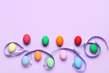 Composition with painted Easter eggs and ribbon on purple background