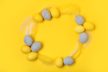Frame made of Easter eggs and feathers on yellow background
