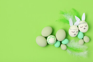 Painted Easter eggs with paper bunny ears and feathers on green background