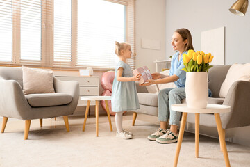 Little girl greeting her mother with gift box at home. International Women's Day