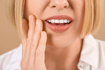 Obraz premium Beautiful mature woman suffering from toothache on brown background,closeup