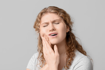 Beautiful young woman suffering from toothache on grey background