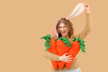 Beautiful young happy woman in bunny ears with carrot-shaped toys on beige background. Easter celebration