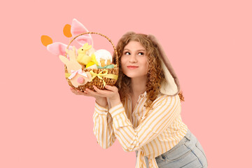 Obraz na płótnie Canvas Beautiful young happy woman in bunny ears with Easter basket on pink background