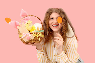 Beautiful young happy woman in bunny ears with Easter basket on pink background