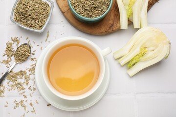 Fennel tea in cup, seeds and fresh vegetable on white tiled table, flat lay