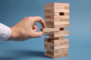 Playing Jenga. Man removing wooden block from tower on blue background, closeup