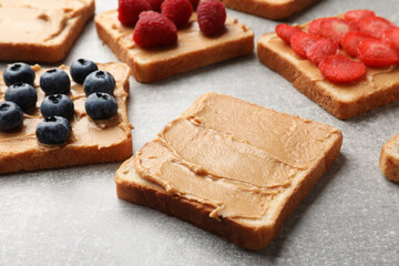 Fototapeta na wymiar Tasty peanut butter sandwiches with fresh berries on gray table, closeup