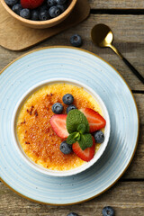 Delicious creme brulee with berries and mint in bowl served on wooden table, flat lay