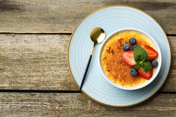 Delicious creme brulee with berries and mint in bowl on wooden table, top view. Space for text