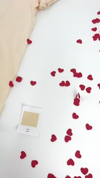 Vertical Video of Little Felt Hearts Falling in Slow Motion Around an Ivory Colored T-shirt on a White Backdrop