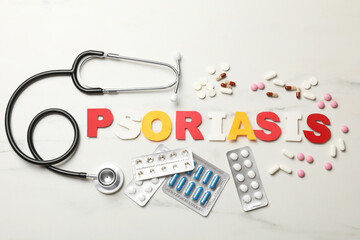 Word Psoriasis made of paper letters, stethoscope and pills on white table, flat lay