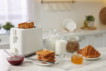 Making toasts for breakfast. Appliance, crunchy bread, honey, jam, milk and croissant on white...