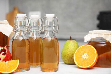 Homemade fermented kombucha in glass bottles and fresh fruits on white table in kitchen