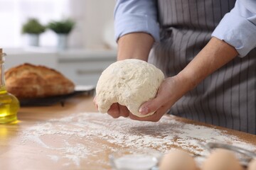 Making bread. Man kneading dough at wooden table in kitchen, closeup